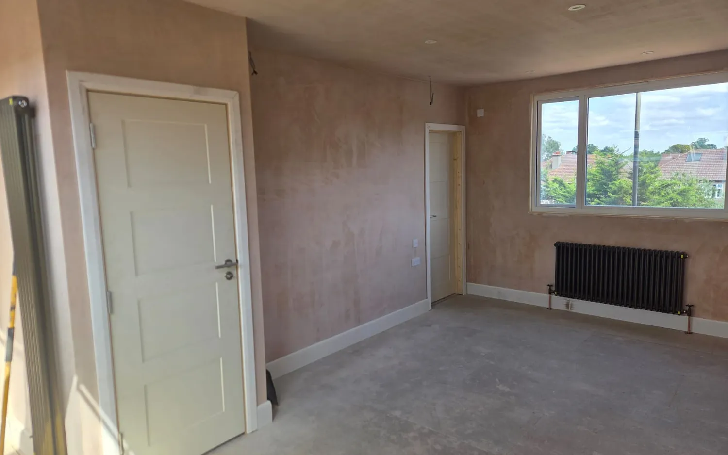 Master bedroom in a Beckenham hip to gable loft conversion, freshly plastered with a large window and column radiator