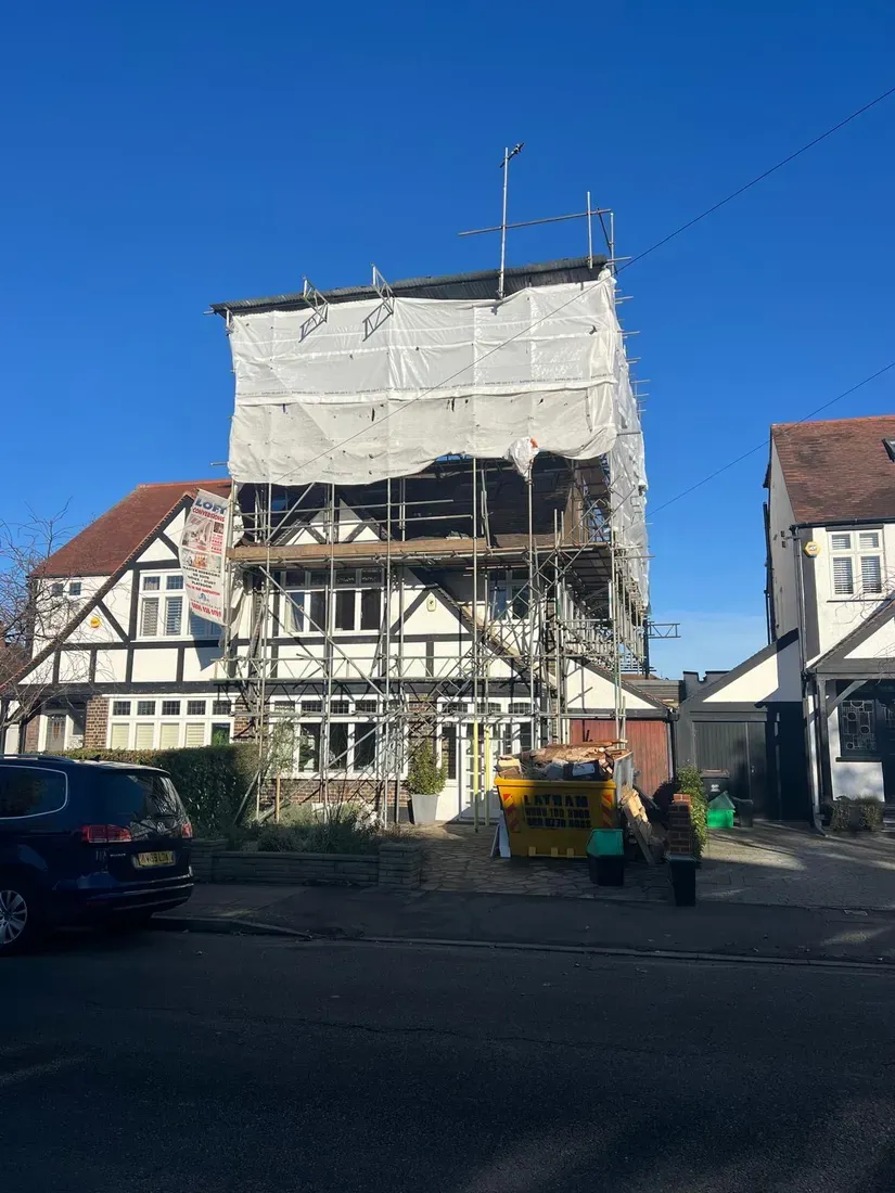 A house wrapped in scaffolding and sheeting during the loft build, with a skip outside