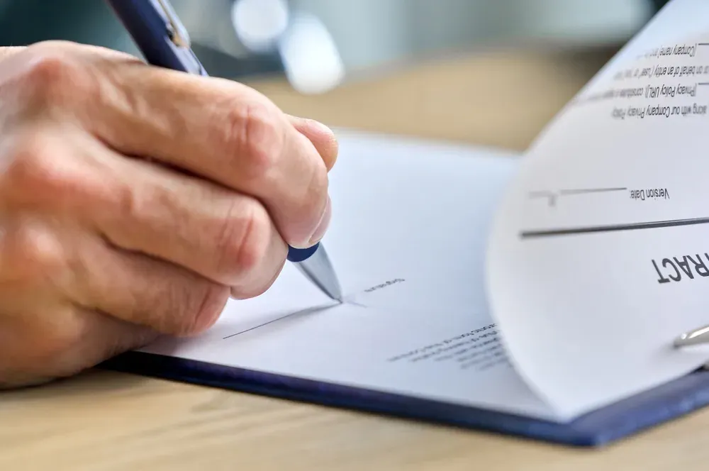 A hand signing a fixed-price building contract